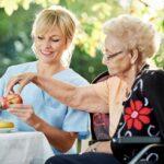 Pflegedienst Guetersloh: Pflegekraft reicht Seniorin im Garten frisches Obst als Teil der taeglichen Betreuung