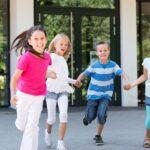 Ferienbetreuung Unternehmen zeigt glückliche Kinder, die lachend vor einem Gebäude spielen